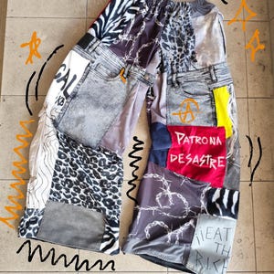 Könnte beinhalten: Weit geschnittene Hose aus verschiedenen Stoffflicken, darunter säuregewaschener Denim, Leopardenmuster, Zebramuster und schwarzer Stoff mit weißem Stacheldrahtmuster. Ein roter Flicken trägt den Text PATRONA DESASTRE und EAT THE RICH.