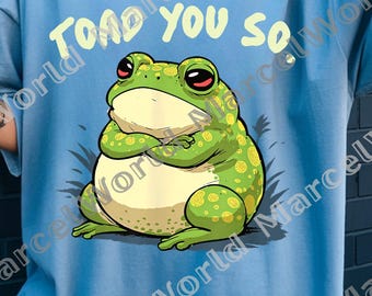 May include: Light blue t-shirt with the text "TOAD YOU SO" above a cartoon frog. The frog is green with yellow spots, red eyes, and crossed arms. The shirt is a casual, oversized fit.