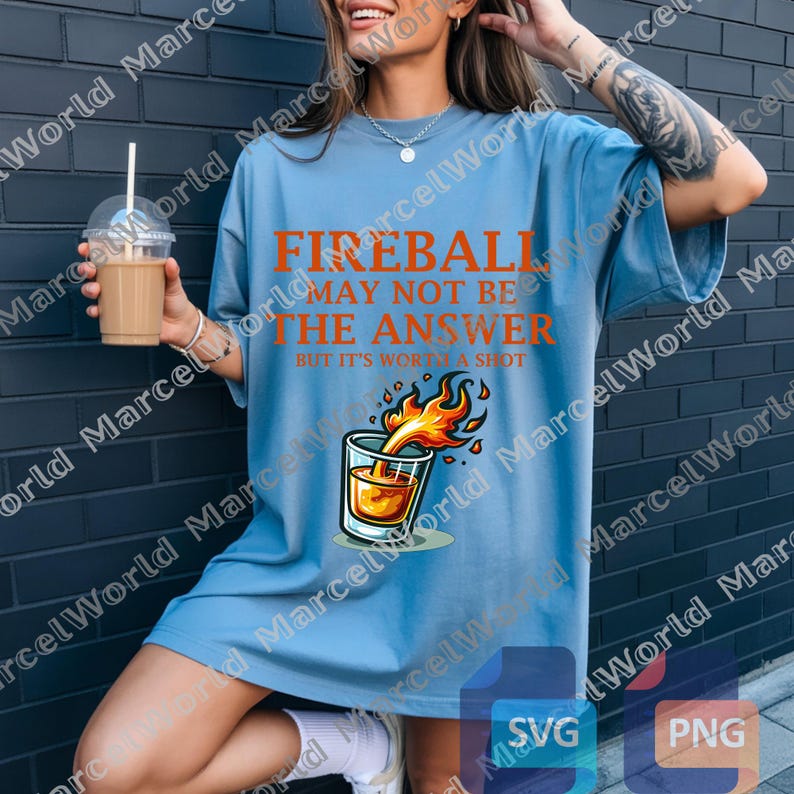 Op de afbeelding: Lichtblauw t-shirt met de oranje tekst "FIREBALL MAY NOT BE THE ANSWER BUT IT'S WORTH A SHOT". Het shirt heeft een afbeelding van een shotglaasje met vlammen. Een casual kledingstuk.