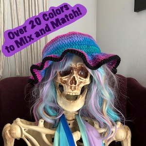 May include: A skeleton wearing a colorful crocheted hat with a black trim. The hat has a wide brim and is made with a variety of colors, including pink, blue, and purple. The text "Over 20 Colors to Mix and Match!" is visible in the image.