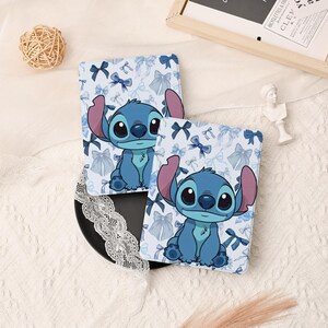 Può includere: Due custodie protettive rettangolari per e-reader o tablet, caratterizzate da uno sfondo azzurro con un motivo ripetuto di fiocchi blu scuro e chiari e un'illustrazione centrale del personaggio blu Stitch con grandi orecchie e occhi scuri.