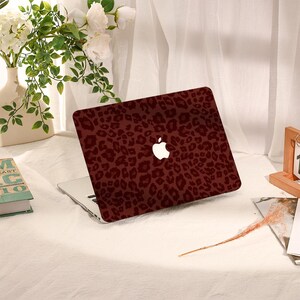 May include: A laptop computer featuring a dark maroon and black leopard print skin on its outer lid. The iconic white Apple logo is clearly visible in the center of the patterned surface, contrasting against the deep red and black animal print design.