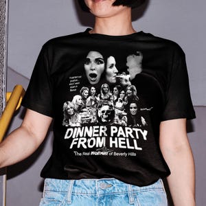 May include: Black t-shirt with a graphic print of a group of women with a skull in the center. The text "Dinner Party From Hell" is printed below the graphic. The text "The Real Nightmare of Beverly Hills" is printed below the title.