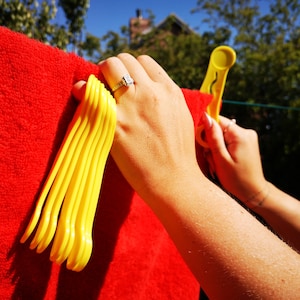 May include: A close-up of a hand holding a bunch of yellow plastic clothes pegs against a red fabric background.