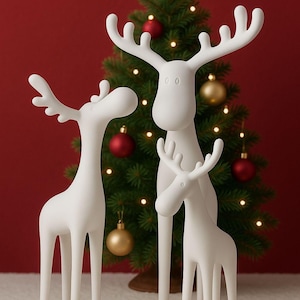 Op de afbeelding: Drie witte rendierfiguren van verschillende groottes staan voor een versierde kerstboom met rode en gouden ballen en een ster. De rendieren hebben lange poten en geweien, wat een feestelijke scène creëert.