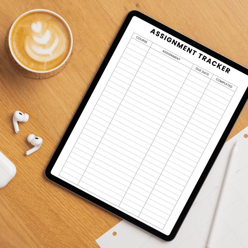 May include: A digital tablet showing an assignment tracker titled "ASSIGNMENT TRACKER". The tablet is on a wooden surface, with a coffee cup featuring latte art, wireless earbuds, and a computer mouse.