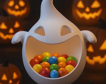 May include: A white ghost-shaped candy dish filled with colorful gumballs, with carved jack-o'-lanterns in the background. The ghost has a smiling face and outstretched arms, perfect for Halloween decorations.
