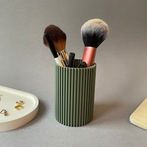 May include: A green ribbed ceramic makeup brush holder with multiple brushes inside.