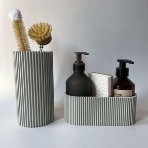 May include: A gray ribbed ceramic bathroom organizer with two soap pumps and a sponge. The organizer has a rectangular shape and is made of a textured material.