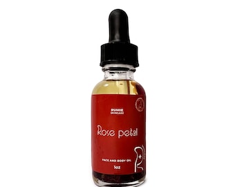 May include: A small glass bottle with a black dropper top filled with a clear liquid. The bottle has a red label with the text "Rumie Skincare Rose Petal Face and Body Oil 1 oz".