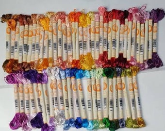 Puede incluir: Una colección de más de 50 carretes de hilo de bordar en una variedad de colores, incluyendo rojo, naranja, amarillo, verde, azul, morado, rosa y blanco. El hilo está enrollado alrededor de carretes de cartón con etiquetas naranjas.