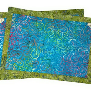 Könnte beinhalten: Zwei blaue und grüne Batik-Platzsets mit grünem Rand. Die Platzsets haben ein Blumenmuster.