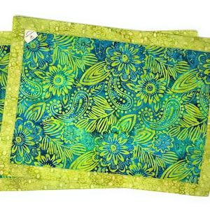 Könnte beinhalten: Zwei grün-blaue Platzsets mit floralem Muster und einem lindgrünen Rand. Die Platzsets haben ein Paisley-Muster.