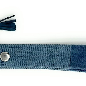 Op de afbeelding: Een blauwe denim sleutelhanger met een zilveren sleutelring en een donkerblauwe kwast.