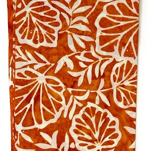 Könnte beinhalten: Orangener Stoff mit einem weißen Blatt-Muster. Der Stoff hat ein Etikett mit der Aufschrift "Batik-107".