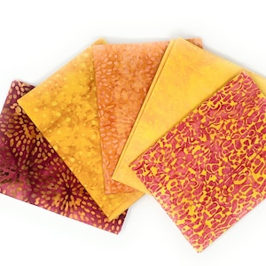 Op de afbeelding: Vijf vierkante stukken stof in verschillende tinten geel, oranje en rood met verschillende patronen. De stofvierkanten zijn in een waaier vorm gerangschikt.