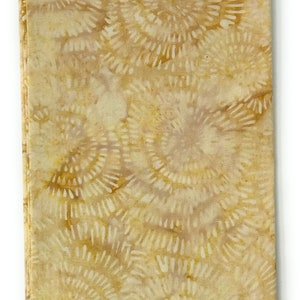 Op de afbeelding: Een gevouwen stuk stof met een batikpatroon van draaiende cirkels in tinten bruin en beige. De stof is gelabeld "Batik-103".