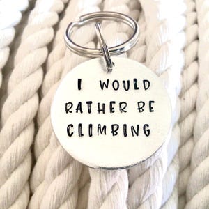 Peut inclure: Porte-clés argenté avec une étiquette ronde qui dit "Je préférerais être en train d'escalader".