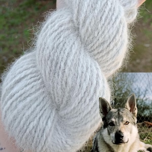 Puede incluir: Una madeja de hilo gris claro, difuso y texturizado, sostenida en una mano. El texto CHIEN LOUP TCHÈQUE está impreso en blanco en la parte superior izquierda. Un perro lobo checoslovaco con pelaje gris, negro y blanco se ve en la esquina inferior derecha.