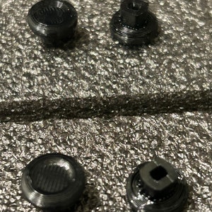 May include: Four black plastic buttons with different shapes and textures. The buttons are designed for use with a gaming controller.