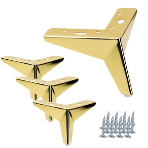 May include: A set of four gold-coloured, angled furniture legs with screw hardware. The legs have a modern, geometric design and are made of a shiny, metallic material. Each leg has a small, white foot on the bottom.
