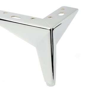 Pode incluir: Uma perna de móvel de metal cromado com base triangular e ponta arredondada. A perna tem vários orifícios para parafusos para fixação em móveis.