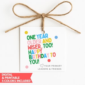 May include: A square white gift tag with a brown twine bow at the top. The text reads ONE YEAR OLDER AND WISER, TOO! HAPPY BIRTHDAY TO YOU! in colorful letters, with small dots and the text YOUR PRIMARY LEADERS & FRIENDS at the bottom right.