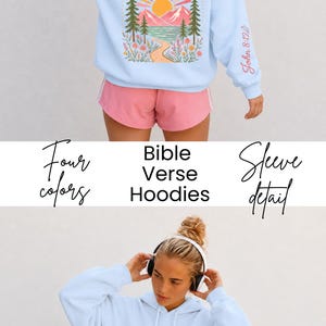 May include: A light blue hooded sweatshirt featuring a back graphic of a sun, mountains, trees, and flowers with the text Walk in His Light. The left sleeve displays the text John 8:12. The front chest features a smaller version of the sun graphic.