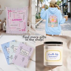 May include: A collage featuring a personalized pink and white striped blanket with the name Lauren, a light blue hoodie with a mountain graphic, three pastel journals titled Dear Paige, and a candle with a label reading Smells like summer!