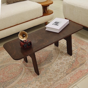 Könnte beinhalten: Ein dunkelbrauner Couchtisch aus Holz mit rechteckiger Platte und abgewinkelten Beinen. Auf dem Tisch steht ein kleiner Plattenspieler im Vintage-Stil sowie ein weißes Buch. Der Tisch steht auf einem gemusterten Teppich.