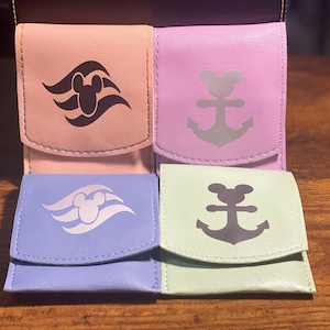 May include: Four small, fabric pouches with different colors and designs. Two pouches feature a black and white Mickey Mouse head with a stylized wave design. The other two pouches feature a black anchor with a Mickey Mouse head on top. The pouches are pink, light blue, lavender, and light green.