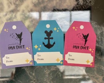 Peut inclure: Trois étiquettes cadeaux avec un fond violet, bleu et rose. Chaque étiquette a un design différent avec une fée, une ancre et une tête de Mickey Mouse. Le texte sur chaque étiquette indique "powered by pixie dust".