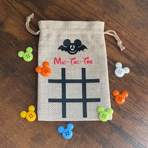 May include: A burlap bag with a black Mickey Mouse silhouette and the words "Mic-Tac-Toe" printed on it. The bag is filled with colorful Mickey Mouse buttons.