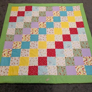 Könnte beinhalten: Eine Patchwork-Decke mit grünem Rand und einer Vielzahl von bunten Quadraten. Die Quadrate bestehen aus verschiedenen Stoffen mit Blumen-, geometrischen und Tupfenmustern.