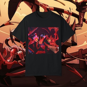 May include: Black t-shirt with a graphic print of three cartoon characters with red and black clothing. The characters are holding weapons and have horns. The background is a dark red with stars.