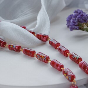 May include: A red and white glass bead necklace with gold accents. The necklace is made of cylindrical beads with a swirling pattern.