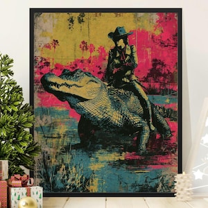 May include: A framed wall art print featuring a stylized illustration of a person wearing a cowboy hat riding on the back of a large alligator. The artwork uses a vibrant color palette of yellow, hot pink, and teal with a distressed texture.