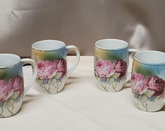 May include: Set of four vintage porcelain mugs with a floral design. Each mug features a pink rose pattern with green leaves and a blue and white background.