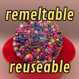 Könnte beinhalten: Eine rote Schüssel gefüllt mit einem klaren, bunten Schleim mit eingebetteten Perlen und Buchstaben. Der Schleim ist mit "remeltable" und "reusable" beschriftet.
