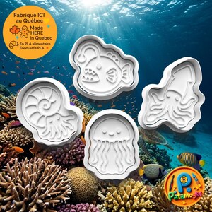 May include: Three white plastic cookie cutters featuring sea creature designs: an anglerfish, an ammonite, and a jellyfish. The cutters are arranged against an underwater coral reef background. Text on the image includes "Fabriqué ICI au Québec" and "Patamogler".