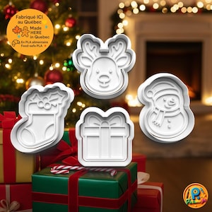 May include: Four white Christmas cookie cutters: a reindeer head, a snowman, a gift box, and a stocking. The cutters are displayed on a stack of wrapped gifts with red and green paper. The background includes a Christmas tree and a fireplace.