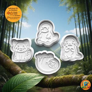 May include: Four white plastic cookie cutters in the shapes of a red panda, platypus, otter, and sloth. The cookie cutters are on a background of a forest scene. The image includes text that says "Made HERE in Quebec".