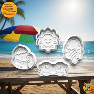 Op de afbeelding: Vier witte plastic koekjessnijders in zomerse vormen: een lachende zon, een ijsje, een zonnebril en een strandscène met een parasol. De snijders liggen op een houten picknicktafel met een strand en oceaan op de achtergrond.