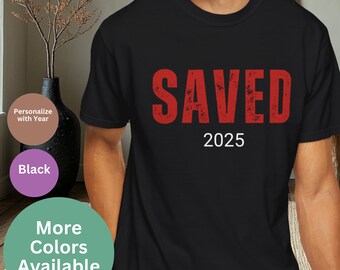 May include: Black t-shirt with the word "SAVED" in red distressed lettering and the year "2025" in white below.
