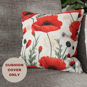 May include: White cushion cover with a red poppy floral pattern. The cushion cover features a large red poppy flower in the center and smaller red poppy flowers around the edges. The background is white with green leaves and stems.