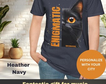 Puede incluir: Una camiseta azul marino jaspeada con un gato negro asomándose desde detrás de la palabra "ENIGMATIC" impresa en naranja. El texto "BRISBANE" está impreso en blanco debajo del gato. La camiseta es un gran regalo para los amantes de la música.