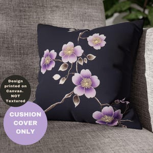 May include: A black cushion cover with a floral design featuring purple flowers with yellow centres. The flowers are arranged on a branch with brown stems and leaves. The text "CUSHION COVER ONLY" is printed in purple on a light purple circle.