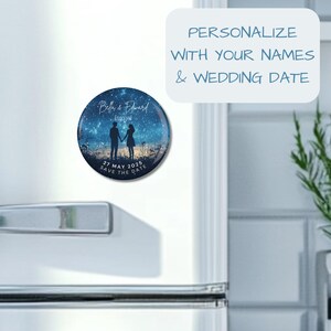 May include: A round save the date magnet with a starry night sky background. The magnet features a silhouette of a couple holding hands, with the text "Bella & Edward Engaged" and "27 MAY 2025 SAVE THE DATE".