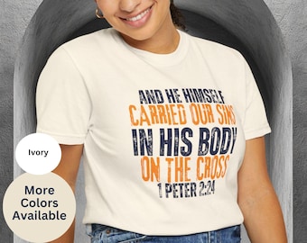 May include: An ivory short-sleeve t-shirt featuring the text AND HE HIMSELF CARRIED OUR SINS IN HIS BODY ON THE CROSS 1 PETER 2:24 in a distressed font, with the words AND HE HIMSELF, IN HIS BODY, and 1 PETER 2:24 in dark blue and CARRIED OUR SINS ON THE CROSS in orange.