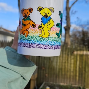 May include: White ceramic mug with a rainbow design and four colorful cartoon bears. The bears are wearing different colored clothing and are standing on a rainbow.